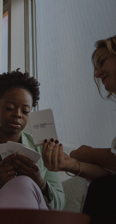 Zwei Personen sitzen im Office und zeigen sich gegenseitig Karten mit einem nicht identifizierbaren Text darauf.